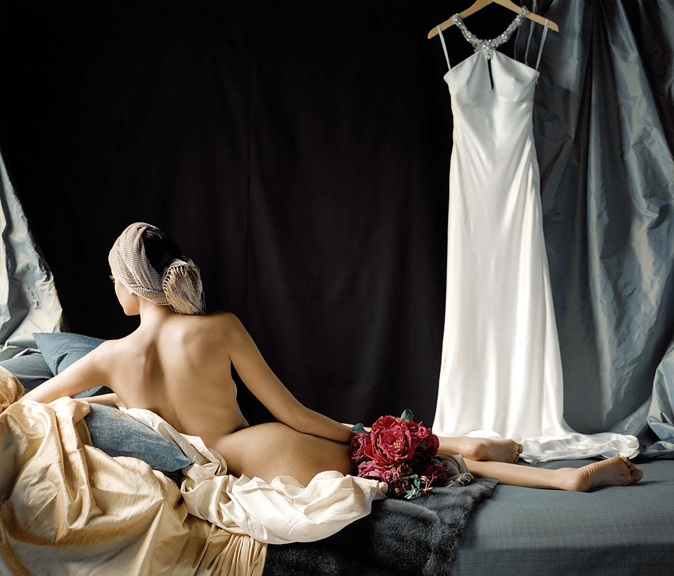 Rodney Smith - A woman lying on a bed with a white dress hanging beside her