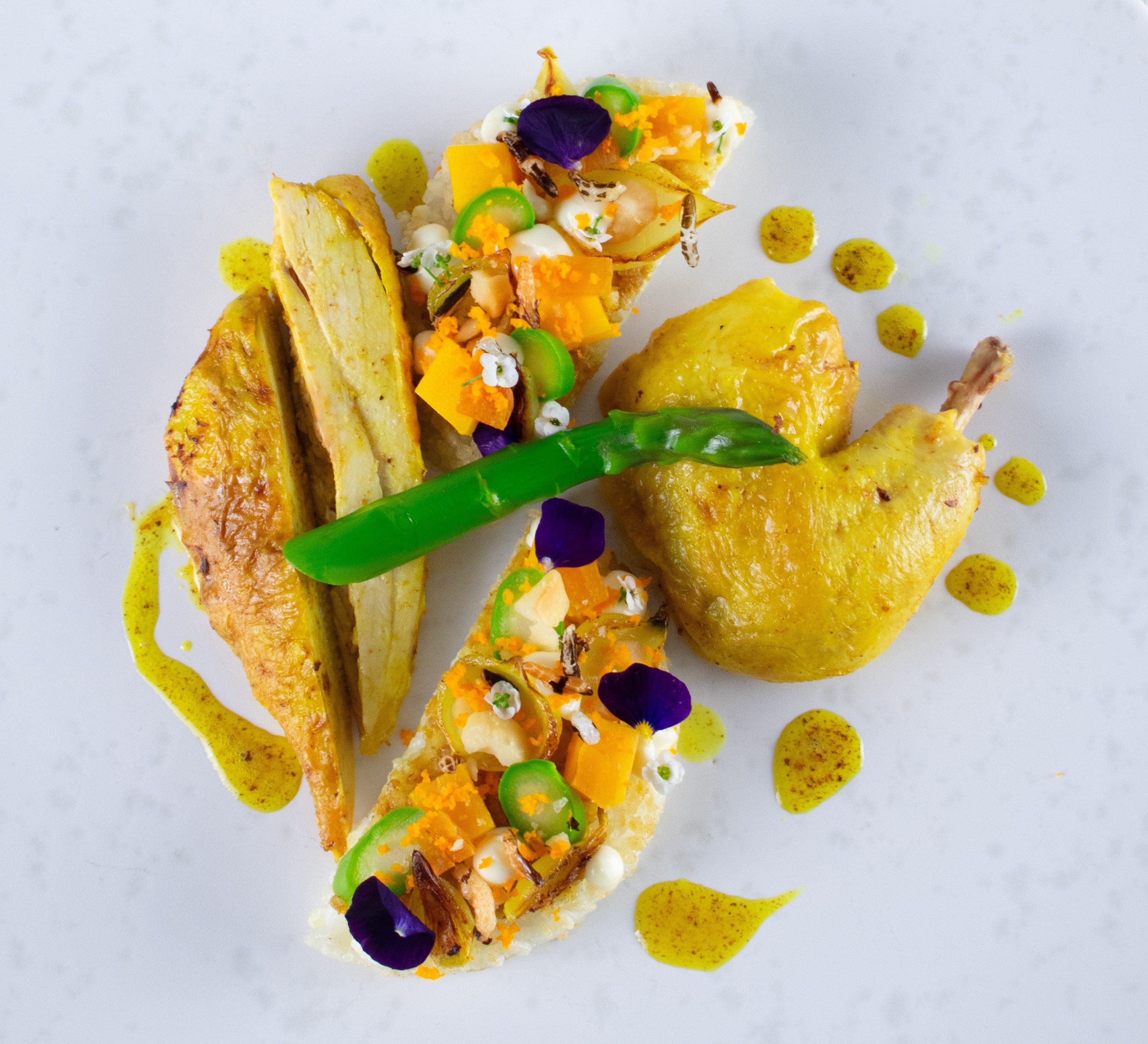 Le Cordon Bleu London - A beautifully plated dish featuring pieces of roasted chicken, vibrant green asparagus, and colourful garnishes including diced vegetables, edible flowers, and drizzled sauce. 