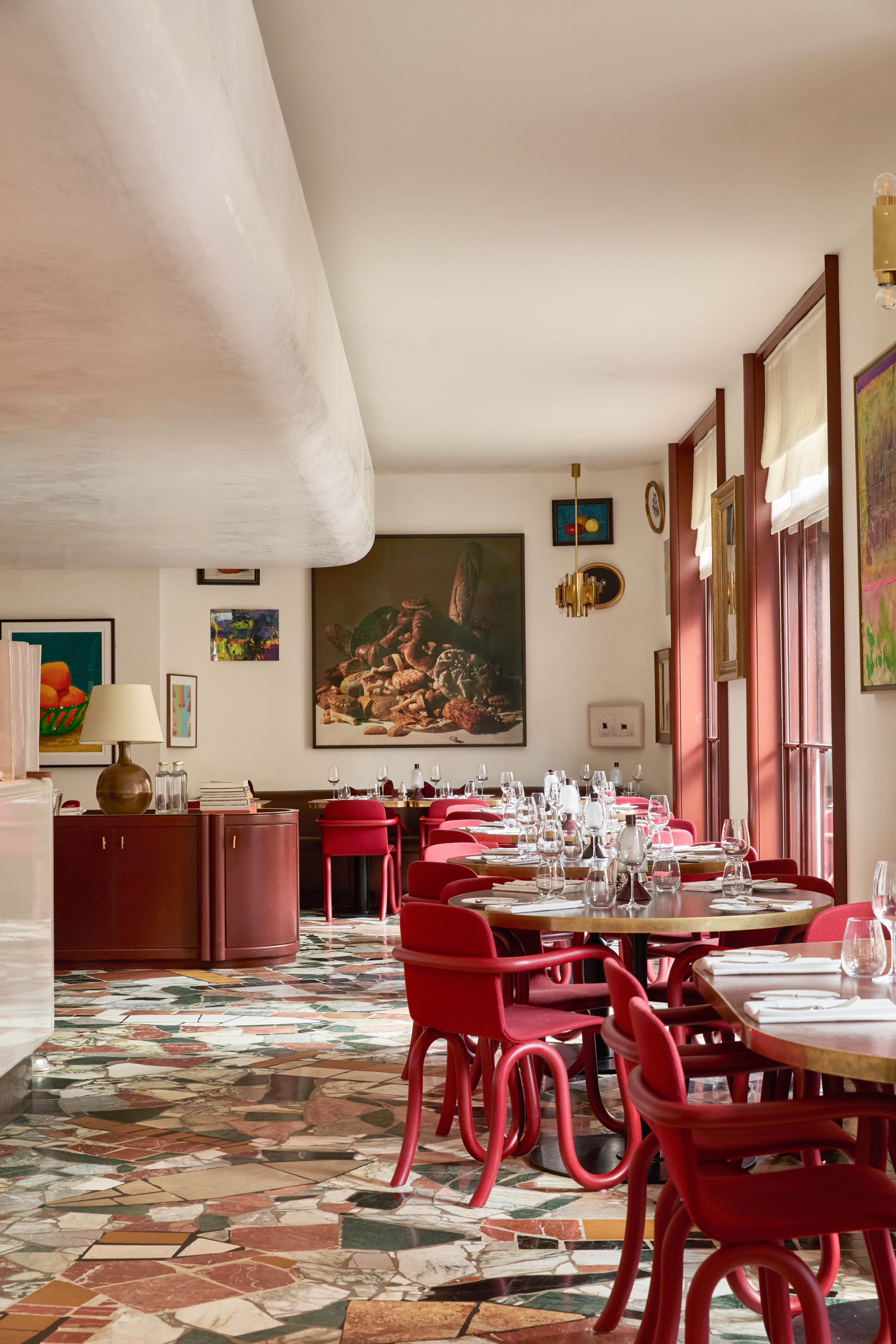 Art restaurants in London - The restaurant interior of Mount St. Restaurant at The Audley featuring round tables, red chairs and a mosaic floor. The space is decorated with eclectic artwork on the walls.