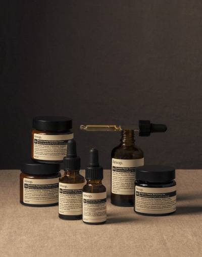 Aesop - brown bottles of skin and hair treatments with white labels and a pipette with product in it